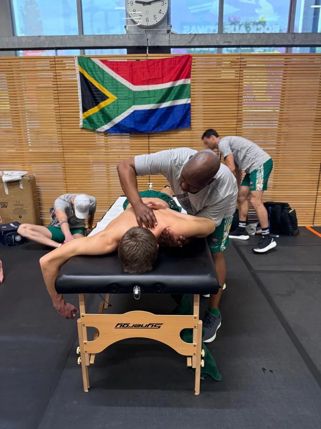 Dan Ntseke performing manual therapy on an athlete beneath the South African flag